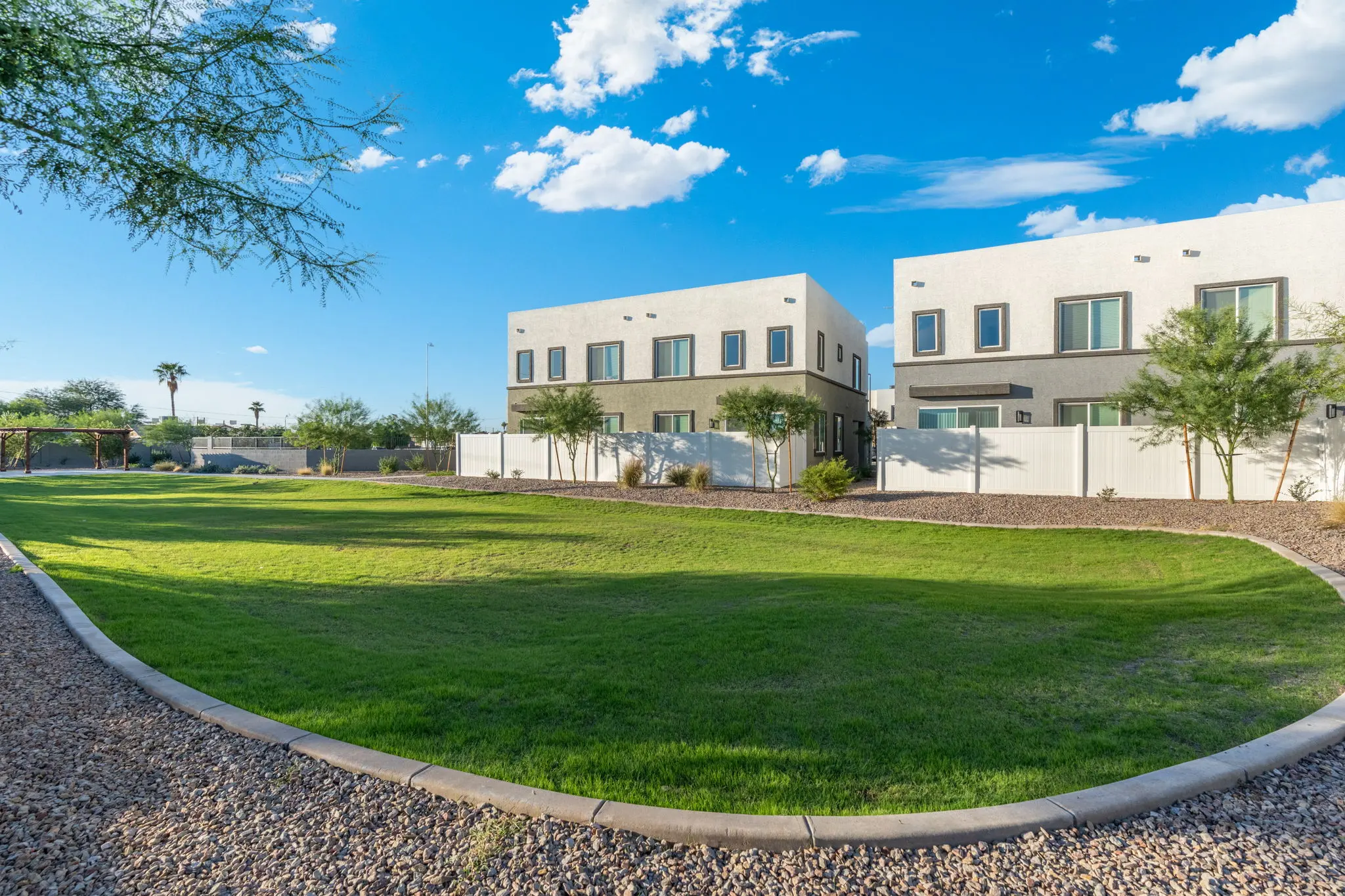 Two modern houses next to a green lawn under a clear blue sky with some clouds.