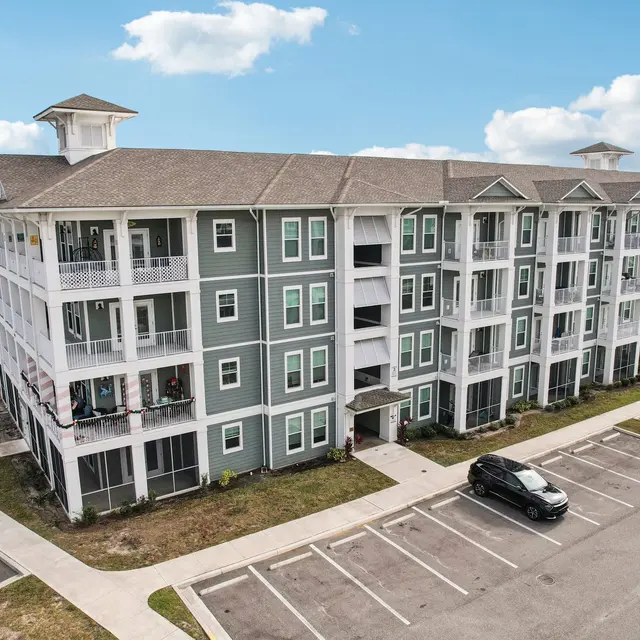 Modern Apartment Complex Aerial view of a multi-story apartment complex with green and white exterior, featuring balconies and a parking area.