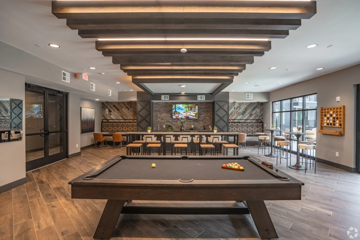 Modern Game Room with Pool Table A modern game room featuring a pool table and a lounge area with tables and chairs, illuminated by stylish ceiling lights. There is a large wall TV and decorative elements in the background.