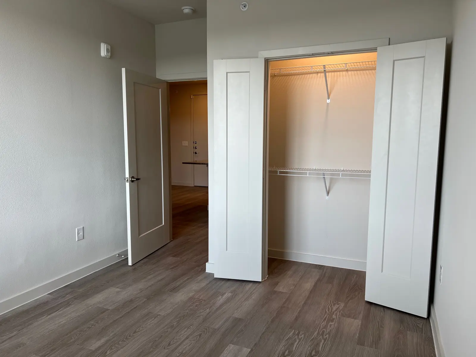 A small room featuring a door leading to the entrance, a closet with open folding doors, and hardwood flooring.