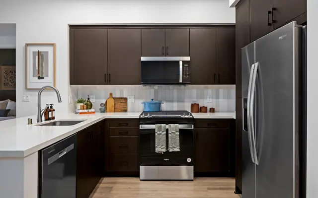 A modern kitchen featuring dark cabinets, stainless steel appliances, and bright countertops. The kitchen includes a gas stove, a microwave, and a dishwasher, with a blue pot on the stove and wooden cutting boards on the counter.