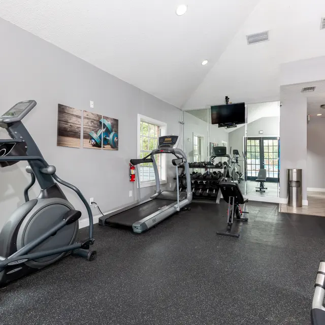 Interior view of a gym with various exercise equipment including two treadmills, an elliptical machine, free weights, and a television.