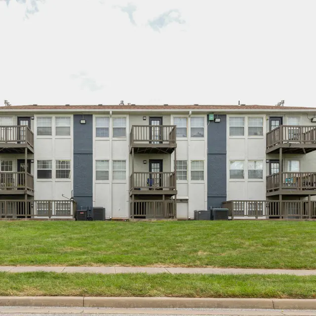 Exterior view of a multi-unit apartment building featuring balconies and a grassy area in front.