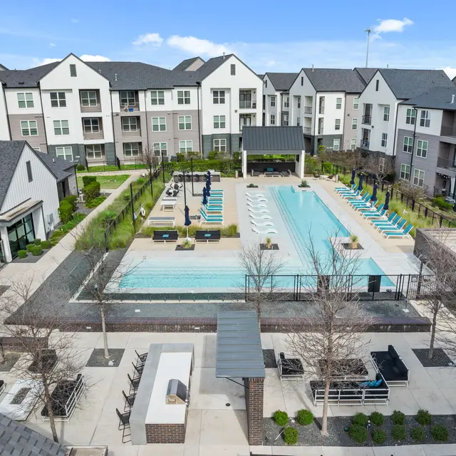 Aerial view of a modern apartment complex featuring a large swimming pool surrounded by lounge chairs and well-maintained landscaping.