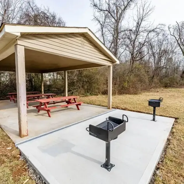 Covered Picnic Shelter with Grills A covered picnic area with red picnic tables and built-in grills in a grassy park setting.