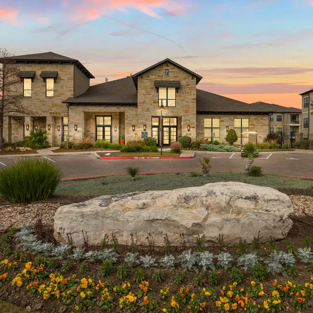 A modern apartment complex with stone architecture and landscaped gardens at sunset.