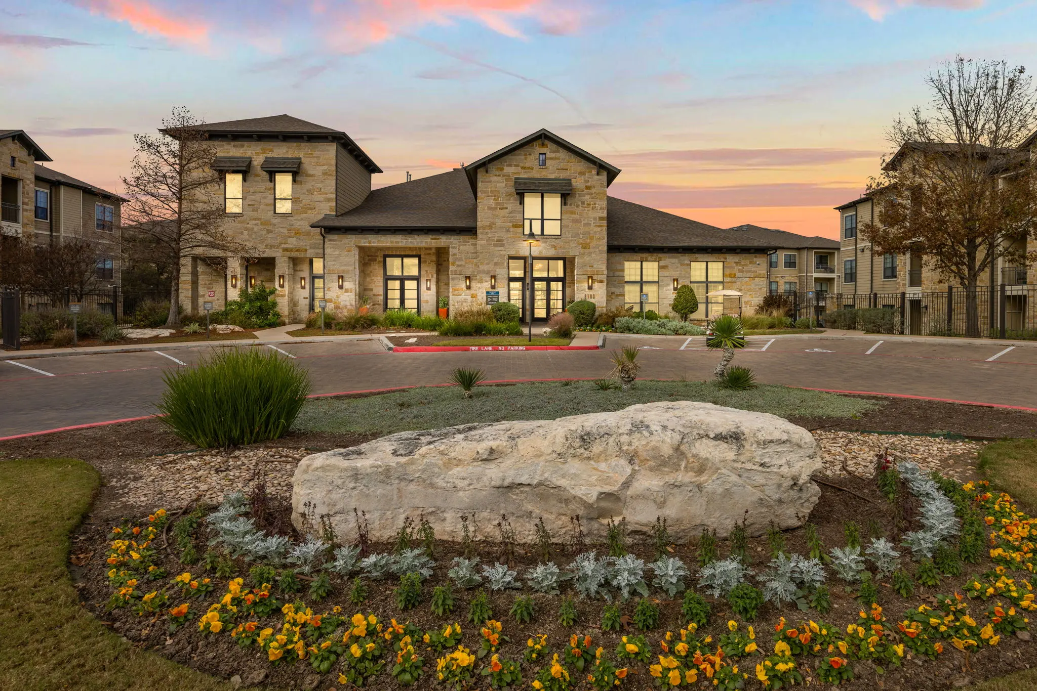 A modern apartment complex with stone architecture and landscaped gardens at sunset.