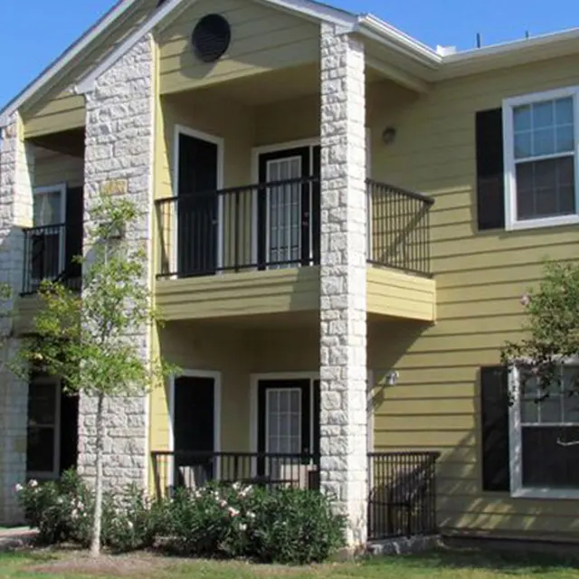 Exterior view of a two-story apartment complex with a yellow facade and stone accents, surrounded by greenery.