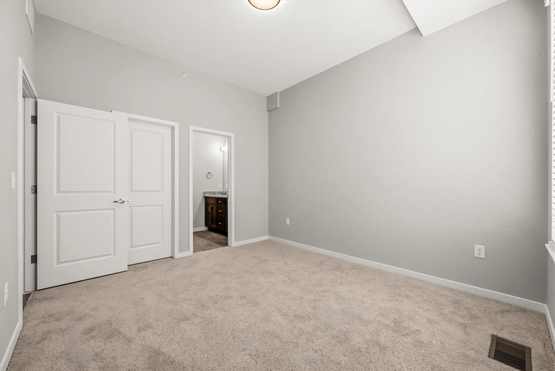 Empty Room Interior A spacious, empty room with carpeted flooring, featuring two white doors leading to a hallway and a bathroom.