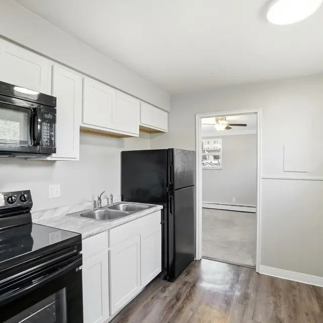 A modern kitchen featuring white cabinets, black appliances including a microwave, stove, and refrigerator, with a gray floor and a door leading to another room.