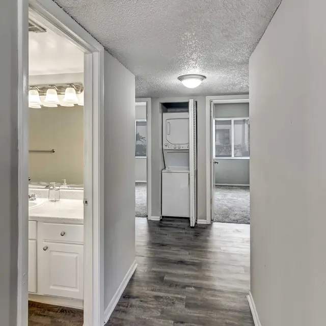 View of a hallway leading to a bathroom and a laundry area with a carpeted living space in the background.