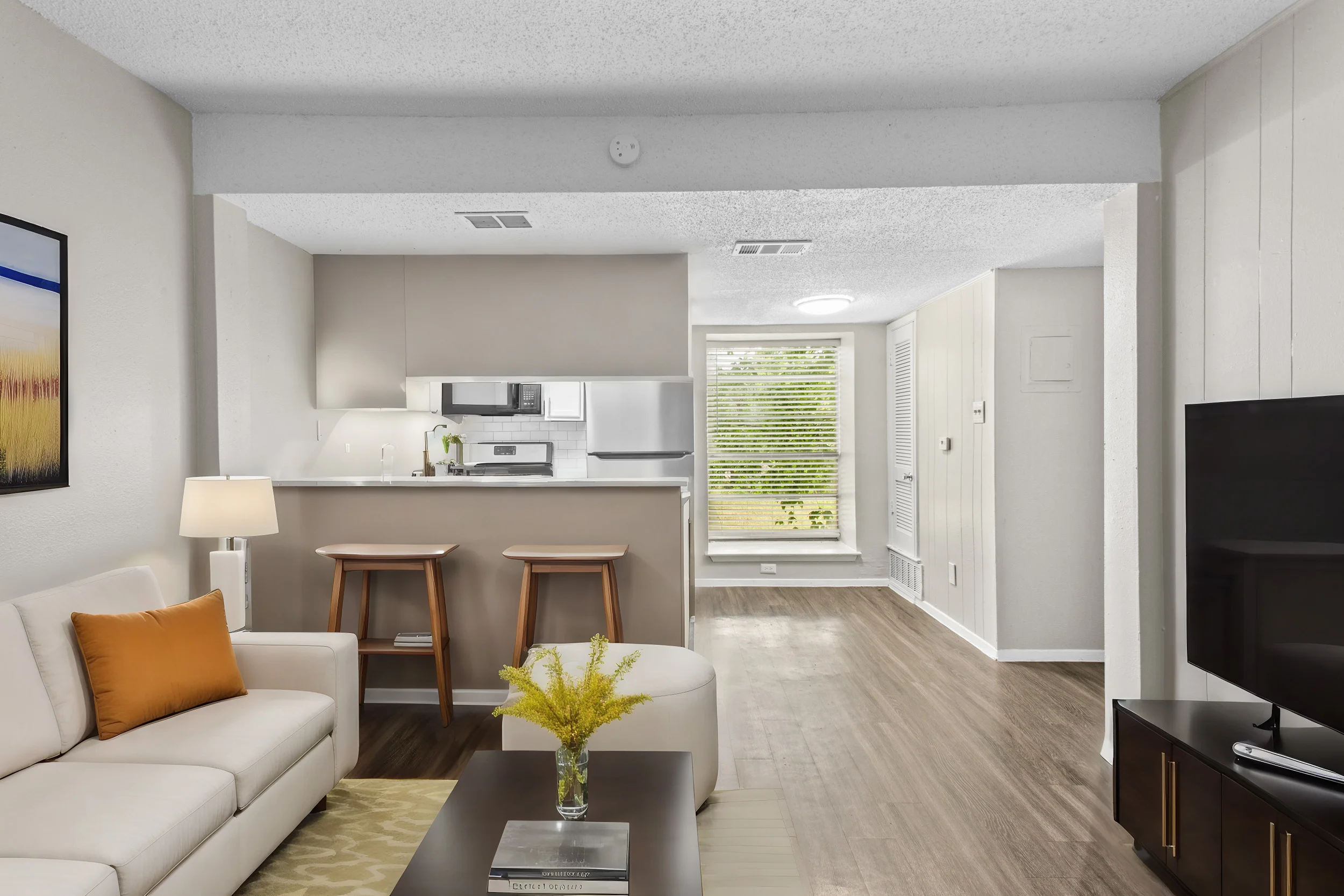 Modern Apartment Living Room and Kitchen A modern apartment interior showcasing a living area with a comfortable sofa, a coffee table, and a bright window. The kitchen area features sleek appliances and bar stools.