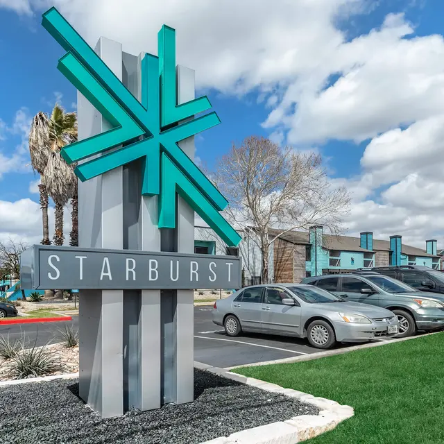 A large sign for 'Starburst' with a modern design, featuring a teal and gray color scheme. The background shows a parking lot with cars and a blue sky with clouds.