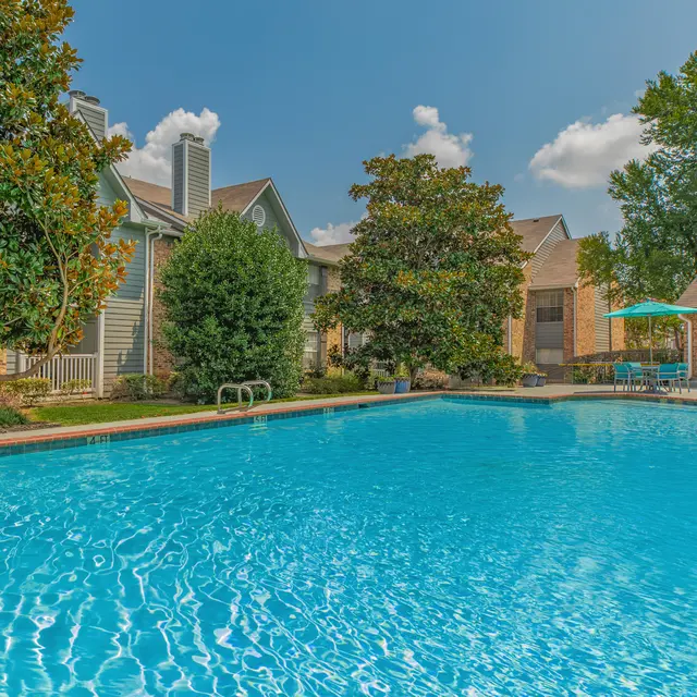 A serene swimming pool surrounded by greenery and buildings under a clear sky.