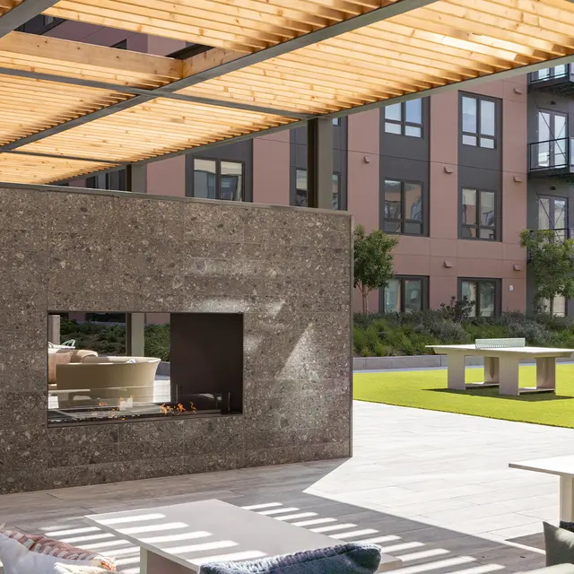 Modern outdoor living area featuring a stone fireplace, comfortable seating, and green grass.