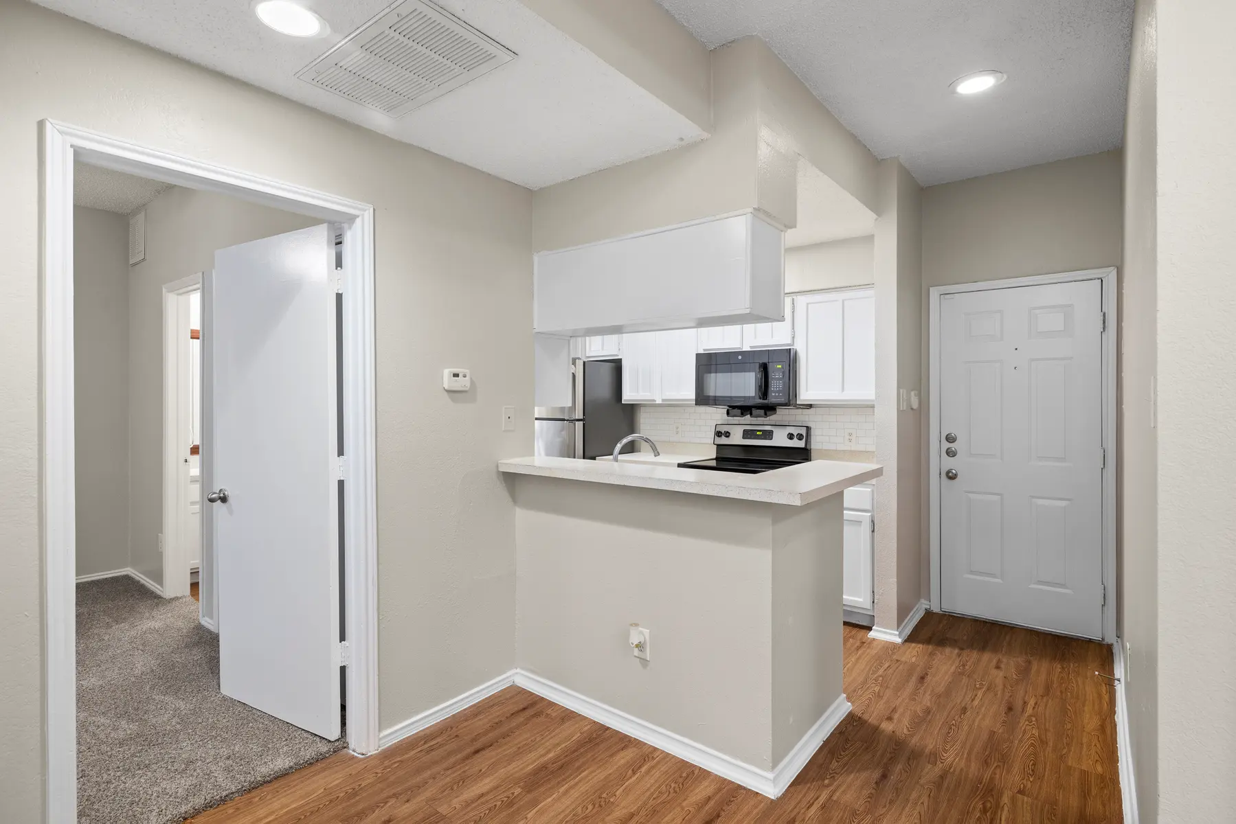 A modern kitchen area connected to a hallway, featuring a bar counter and white cabinetry.
