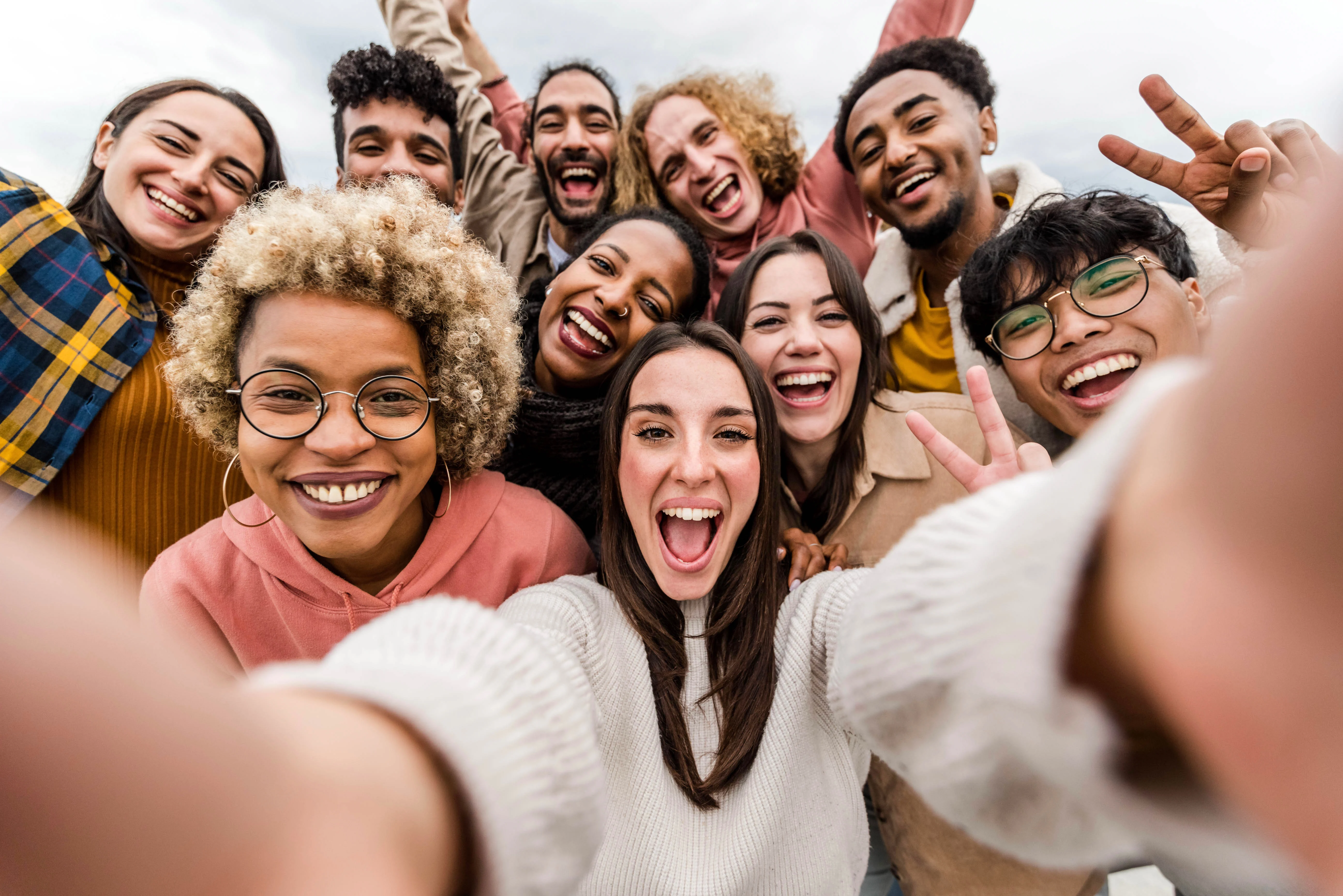 Joyful Group Selfie A group of diverse young adults taking a selfie outdoors, smiling and posing joyfully with a clear blue sky in the background.