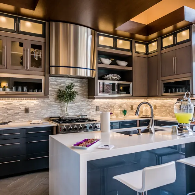 A modern kitchen featuring sleek cabinetry, stainless steel appliances, and a large island with seating. The space is illuminated by soft lighting and has large windows offering natural light.