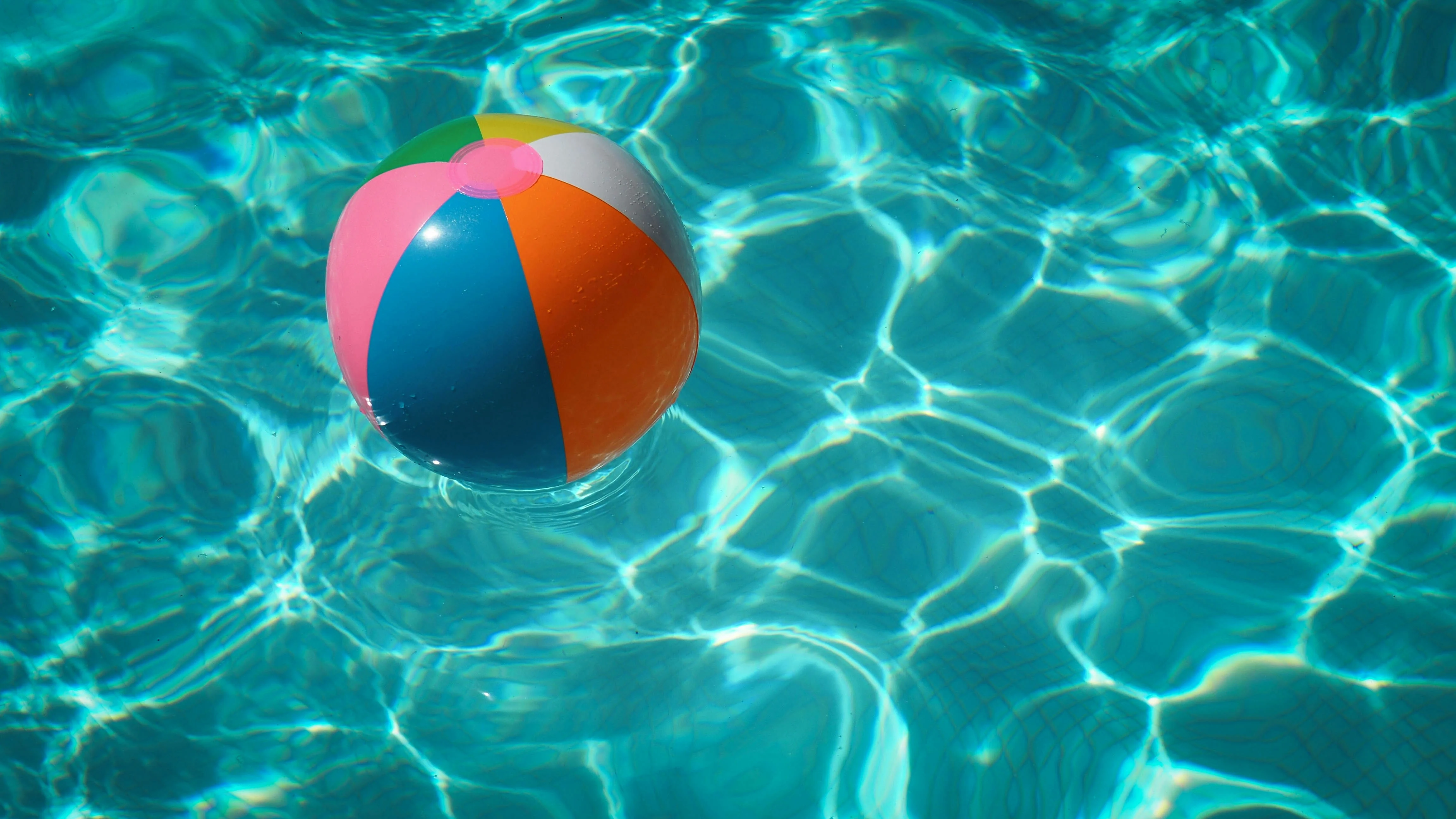 A colorful beach ball floating on the surface of a clear blue swimming pool.