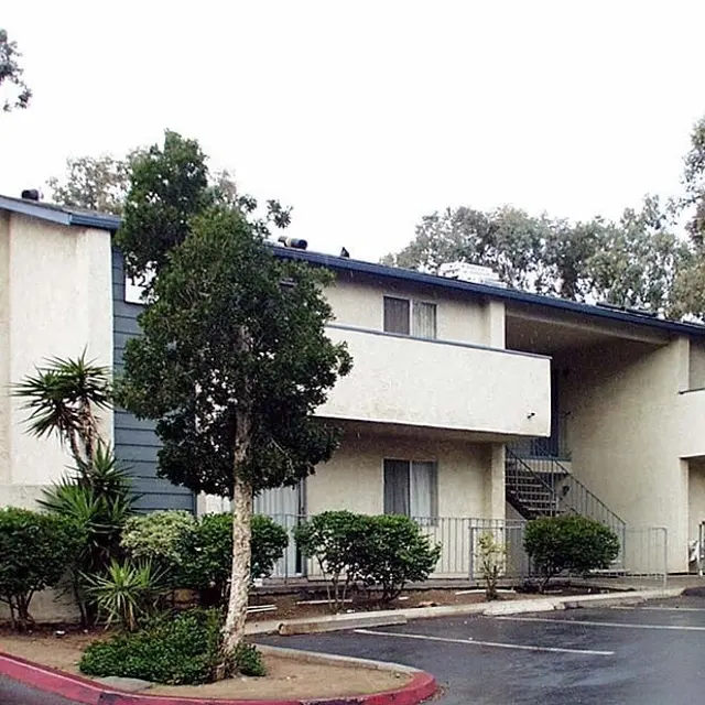 Two-Story Apartment Complex A two-story apartment complex surrounded by trees and landscaping on a rainy day.