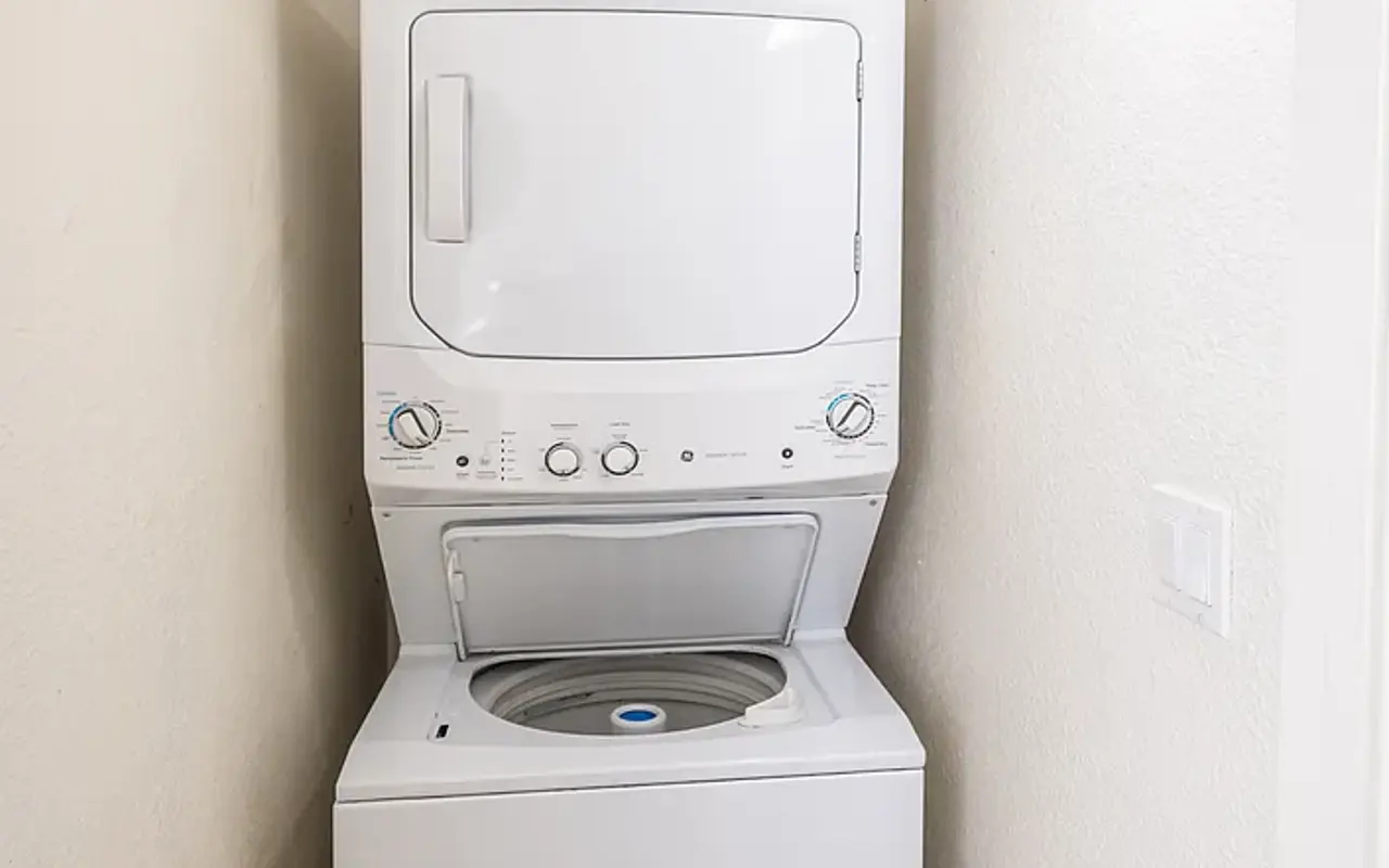 A compact laundry area featuring a stacked washer and dryer unit against a light-colored wall with a light fixture above.