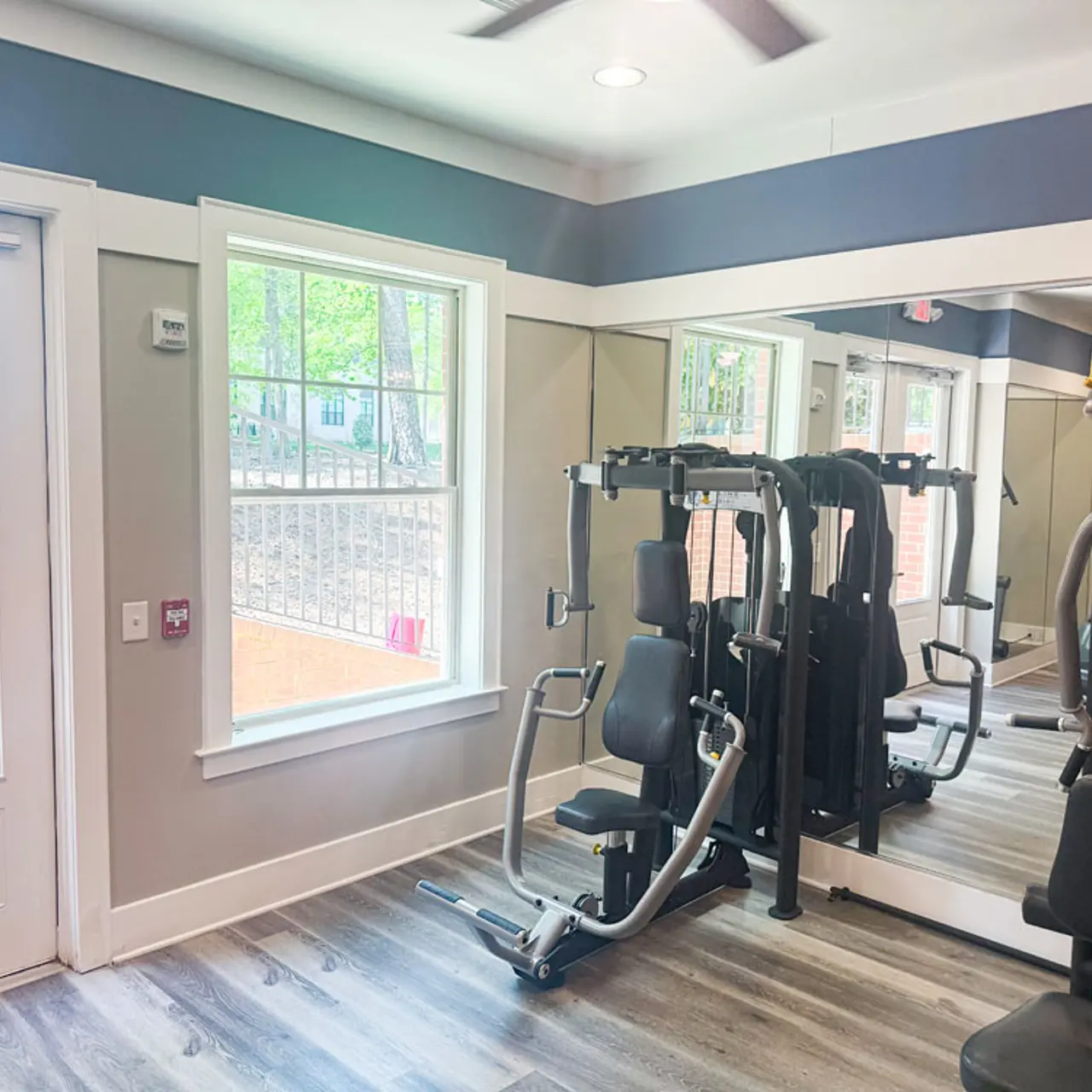 Interior view of a gym featuring exercise equipment, large windows, and wooden flooring.