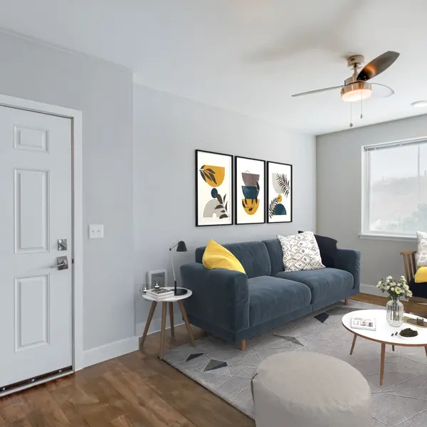 A bright, modern living room with a comfortable sofa, minimalist decor, and a large sliding glass door opening to a balcony. The space includes wood flooring, a ceiling fan, and simple wall art.