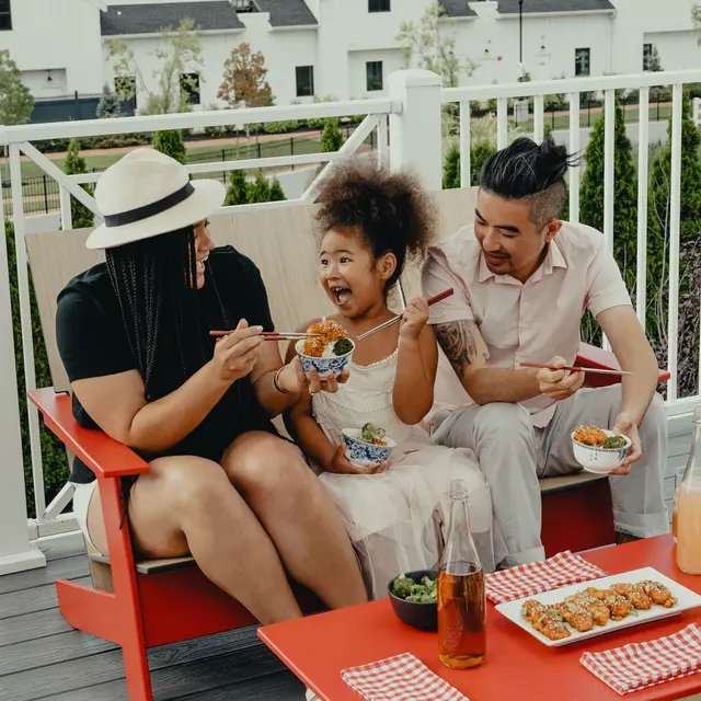 High Street Lofts A family enjoying a meal outdoors on a deck, sharing food and laughter, with a view of modern homes in the background.