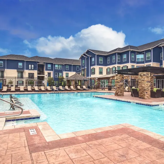 Student Housing in Columbia, MO - The Den - Pool with Deck, Submerged and Poolside Lounge Seats, and Pergola.