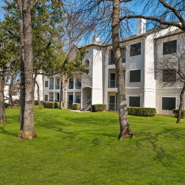 Arboretum at Lewisville apartment buildings in Lewisville, TX, surrounded by mature trees and a well-maintained green lawn.