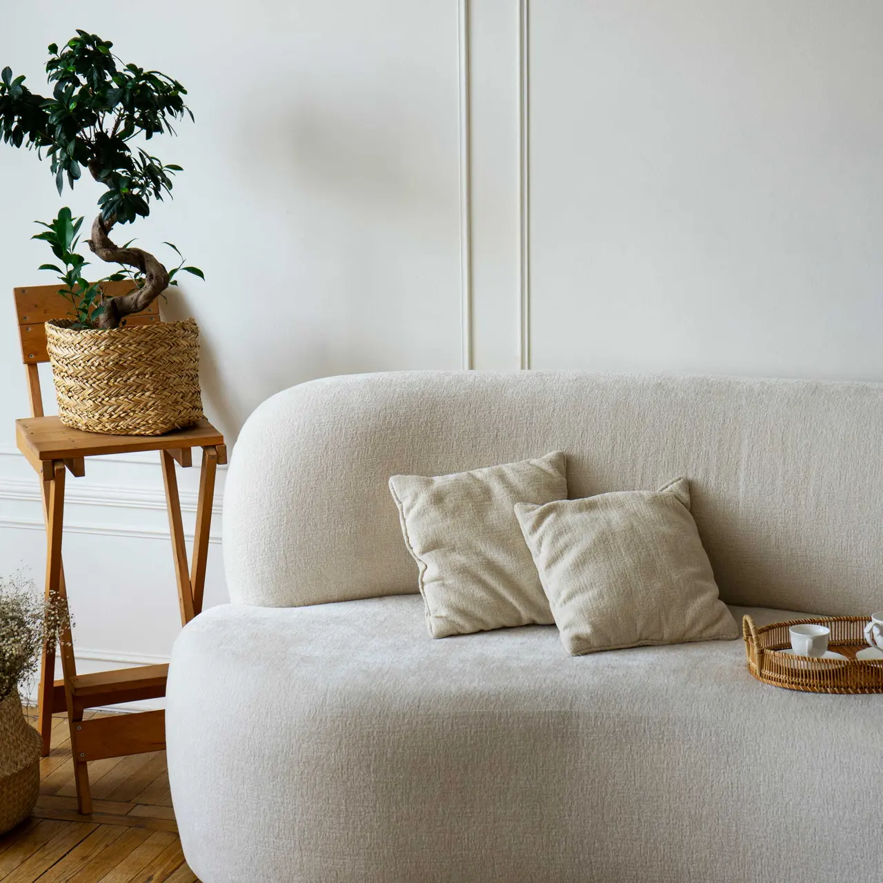 Cozy Modern Living Room A modern living room featuring a light-colored couch with two cushions, a small wooden side table with a potted plant, and a wicker basket holding dried flowers.