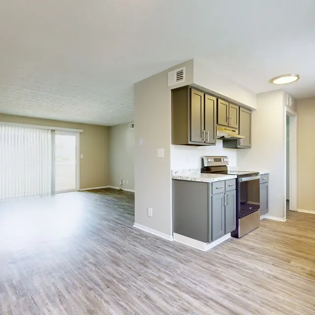 The Hideaway -  A spacious and modern open-plan living area featuring a kitchen and a living room. The kitchen includes gray cabinets and light countertop, while the living area has large windows with curtains and light-colored walls.