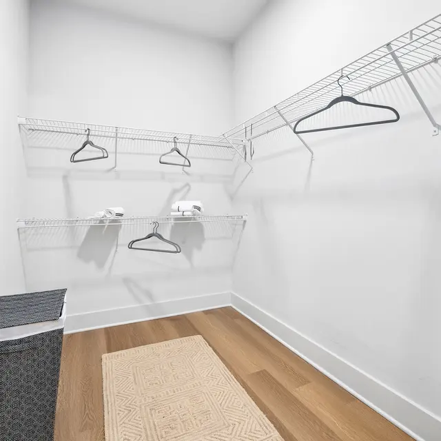 An empty closet area with wire shelving, hangers, a laundry basket, and a small rug.