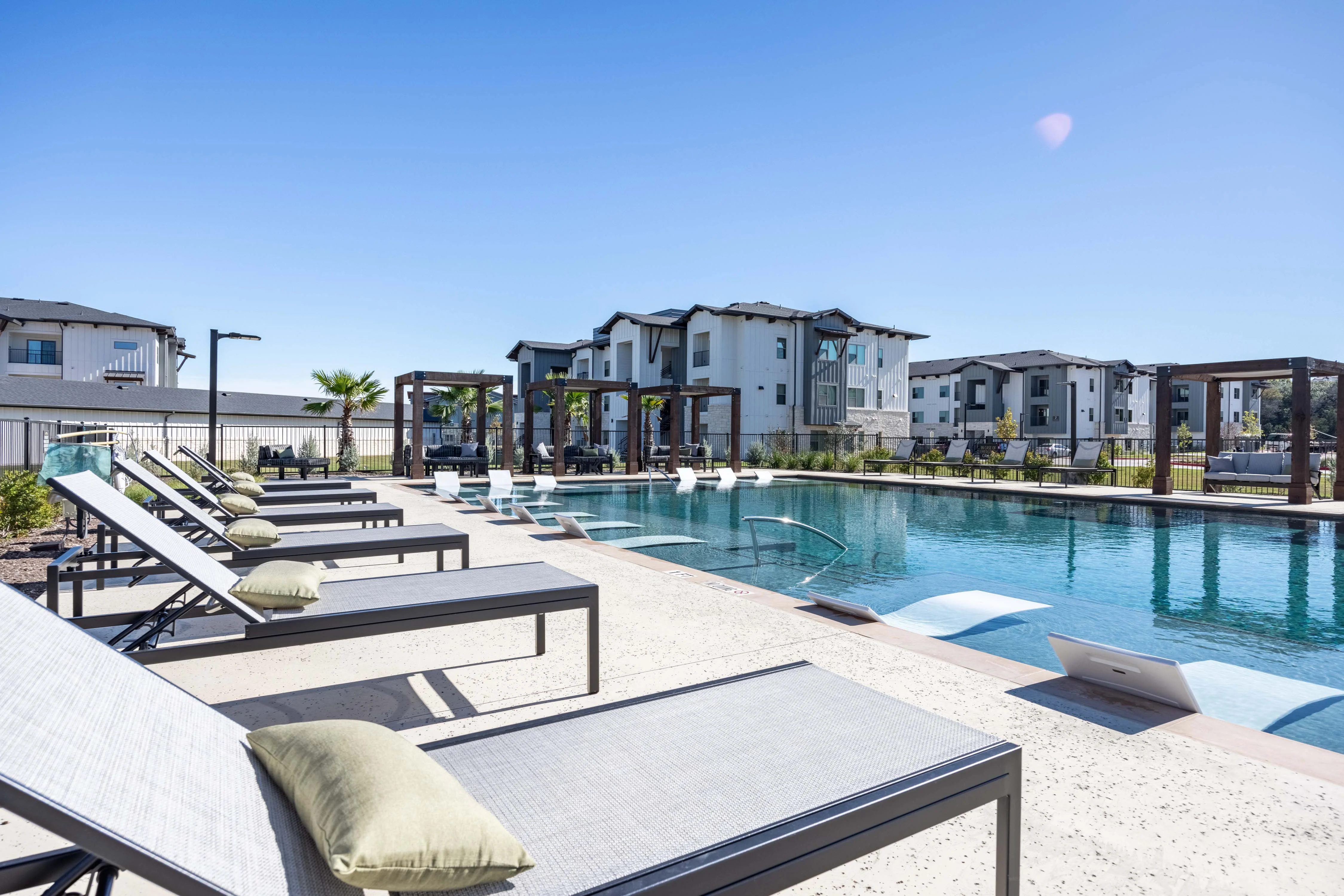 A modern pool area with lounge chairs beside a clear blue pool and stylish apartment buildings in the background.