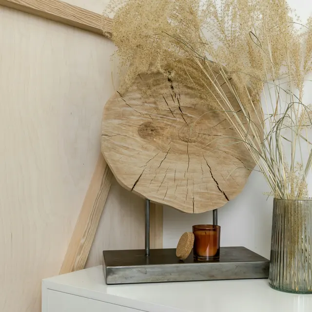 Stylish Decor Arrangement with Wood and Dried Plants A wooden slice displayed on a metal stand alongside a small candle and a vase filled with dried plants.