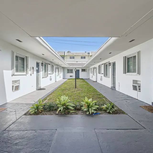 View of a motel courtyard featuring a central grassy area and surrounding rooms with doors numbered 1 to 8.