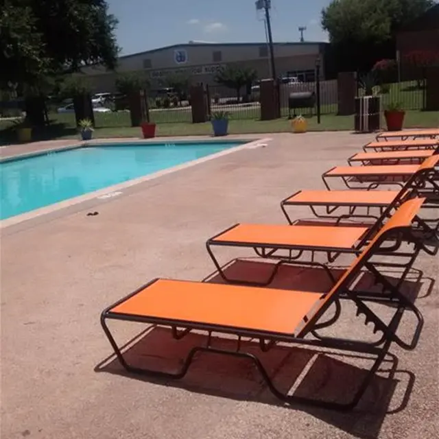 A sunny pool area with an empty swimming pool and several orange lounge chairs lined up beside it.