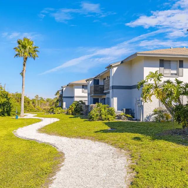 Scenic Pathway to Beachfront Accommodations A scenic pathway leading through greenery to buildings near the beach, with a clear blue sky.