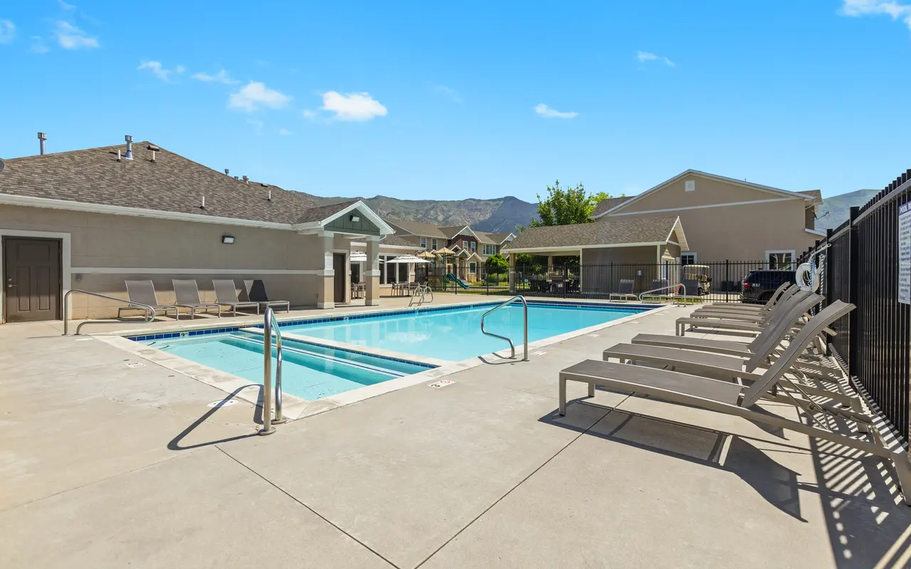 Inviting Poolside Area A clear blue pool surrounded by lounge chairs, with a clubhouse and mountains in the background under a bright blue sky.