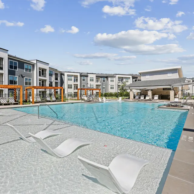 A clear swimming pool with lounge chairs beside it, surrounded by modern apartment buildings.