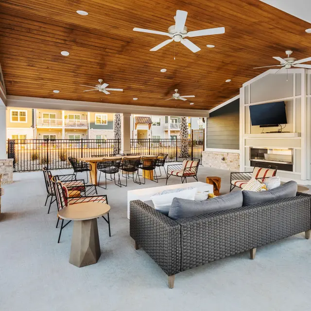 Modern Outdoor Lounge Area An outdoor lounge area featuring a ceiling fan, comfortable seating, a coffee table, and a television on the wall, surrounded by brick pillars.