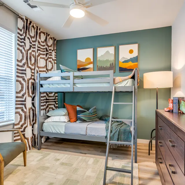 A cozy children's bedroom featuring a bunk bed, green accent wall, and modern decor with artwork and a stylish lamp.