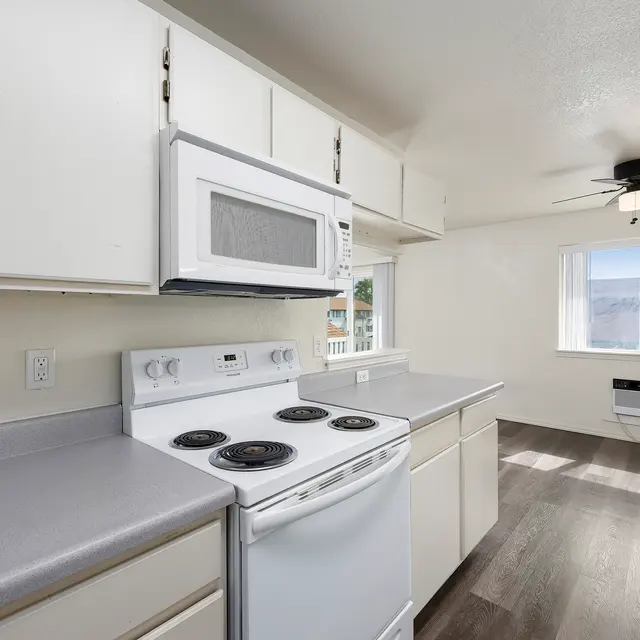 Modern Kitchen Interior A modern kitchen featuring white cabinets, a white stove, and a microwave. One window provides natural light, illuminating the gray countertop and dark flooring.