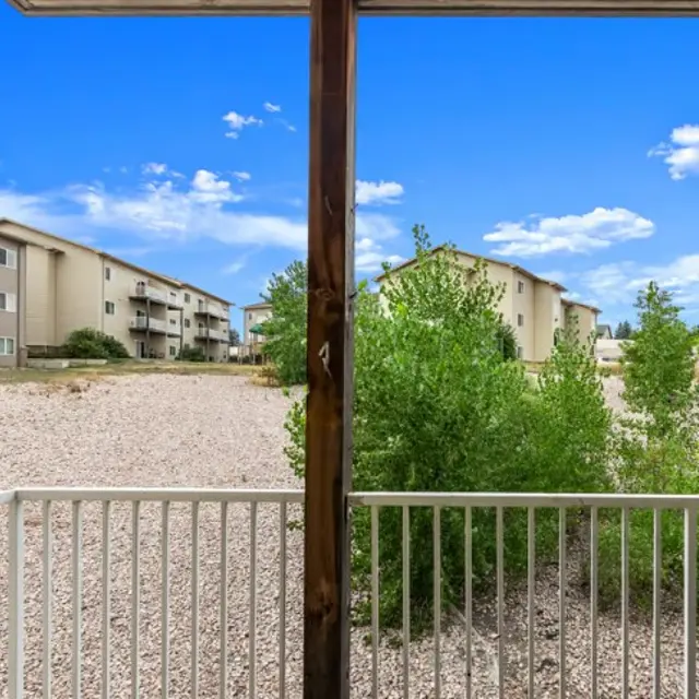 Eagle Ridge View of apartment buildings and gravel area from a balcony with a white railing; clear blue sky in the background.