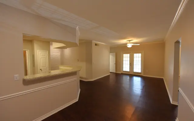 Spacious room with hardwood floors, light walls, a ceiling fan, and an open kitchen area with a bar counter.