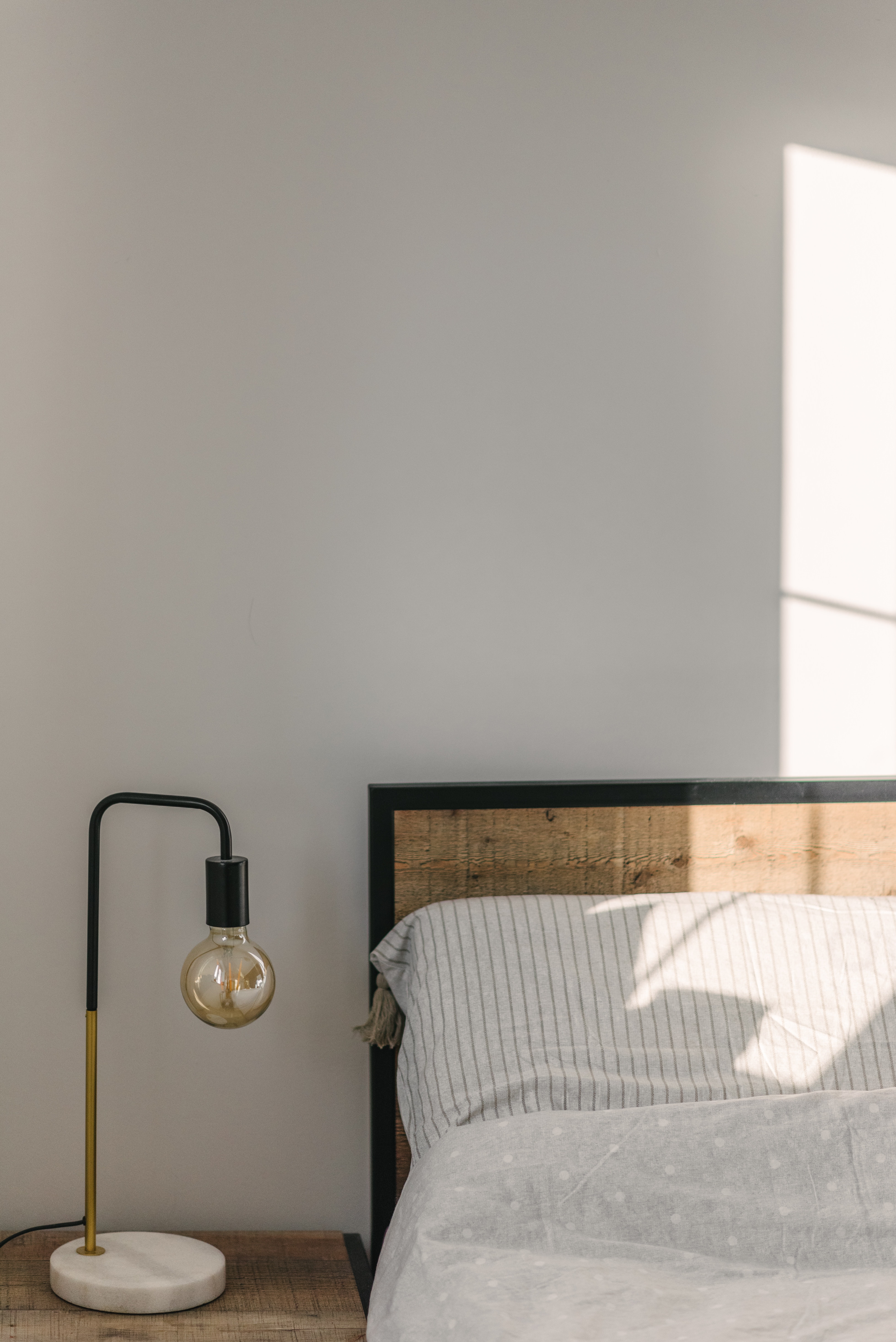 Minimalist bedroom with a wooden headboard, striped bedding, and a sleek lamp beside the bed