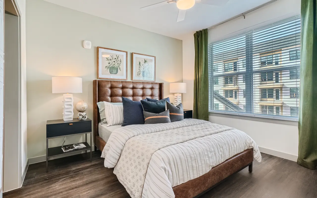 A bedroom at Standard on the River with a bed, a bedside table with a lamp on each side, hardwood flooring, and a window.