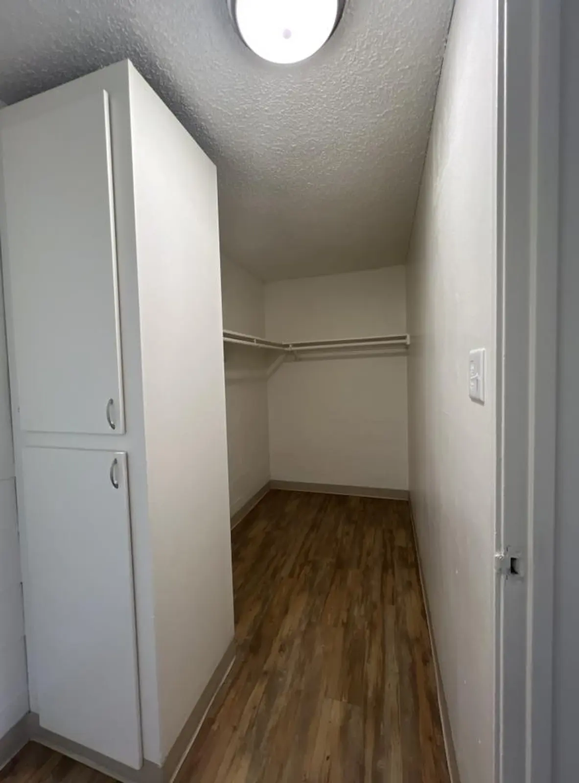 Walk-in closet with hanging rails, upper shelves and open cabinet doors.
