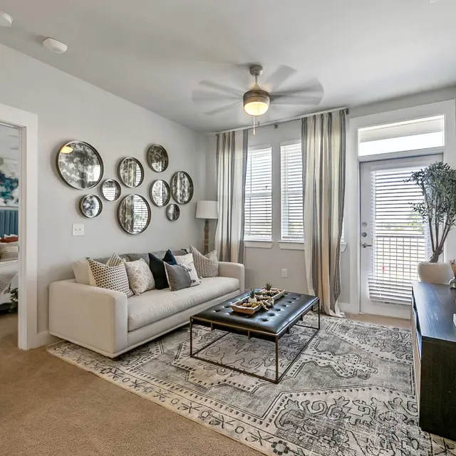 Modern living room with a sofa, decorative mirrors on the wall, a coffee table, and large windows, showcasing a cozy atmosphere.