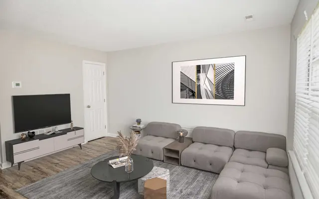 Summit at 501 Modern living room featuring a gray sectional sofa, round coffee table, television, and artwork on the wall. Bright and airy feel.